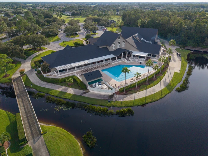 Aerial view of a clubhouse and pool terrace beside a lake