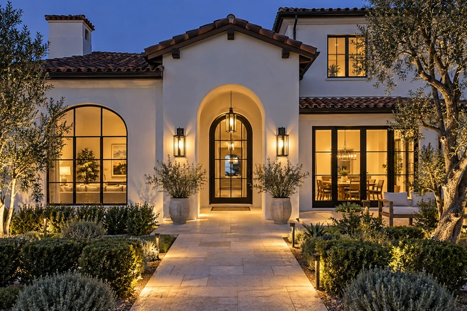 White stucco house at twilight with illuminated entry sconces and a softly lit path, every architectural edge tack sharp